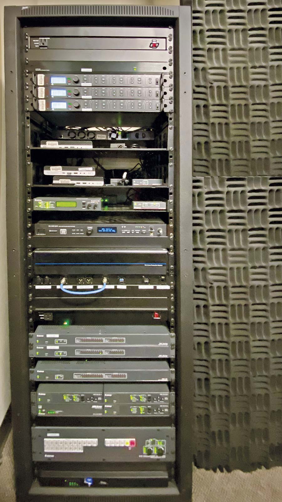 The AV system components, such as the DTP CrossPoint 108 4K IPCP MA 70 matrix switcher and the three DMP 128 audio processors, are rack-mounted within the control room - interior.