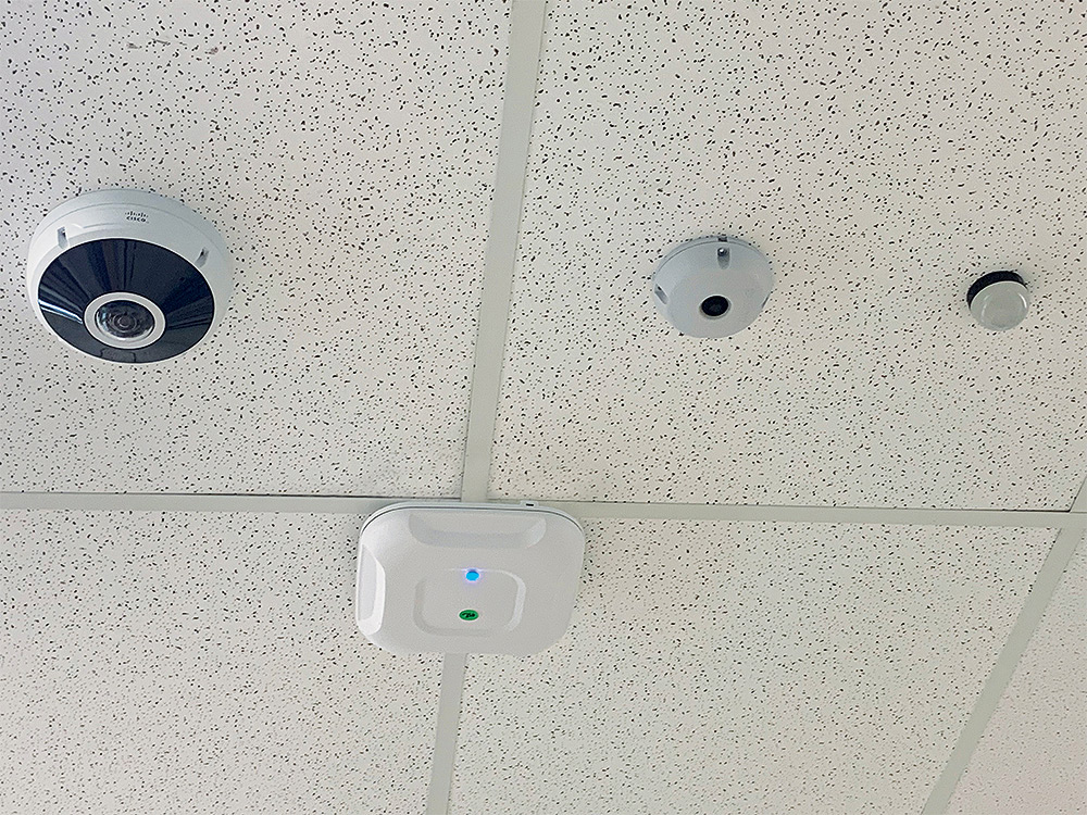 Classroom surveillance camera and Recording-in-Progress light share ceiling space with motion sensor and WiFi access node.