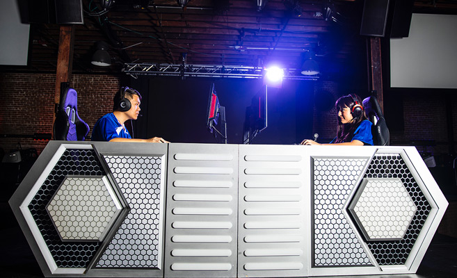 Two students competitively playing a video game on a stage.