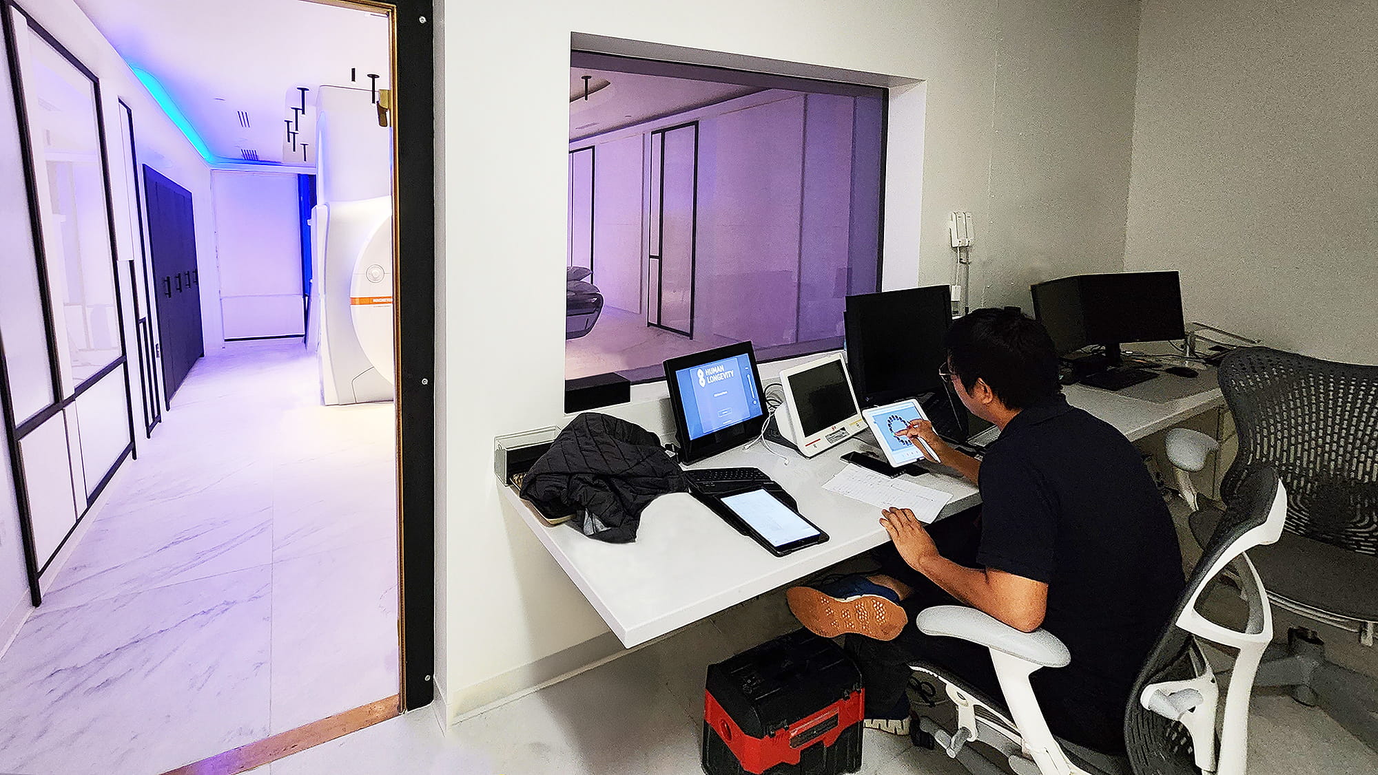 Technicien d'AV Structural finalisant la configuration d'un écran tactile à l'extérieur de la salle d'IRM, où l'automatisation et les contrôles de confidentialité sont gérés via des interfaces Extron.