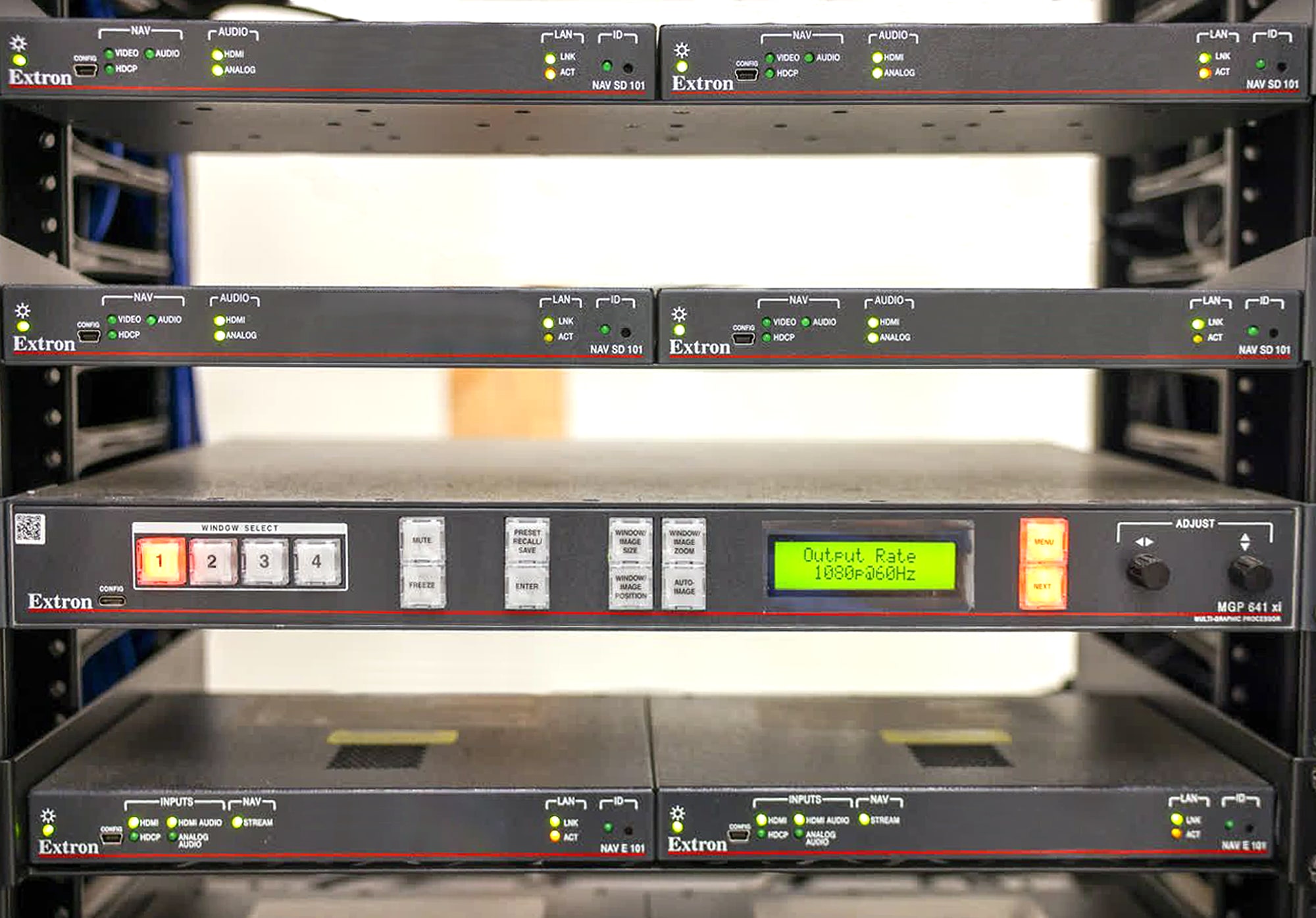 Des encodeurs, décodeurs NAV avec scaler, MGP 641, switches réseau, et autres équipements audiovisuels dans des racks situés dans le local technique.