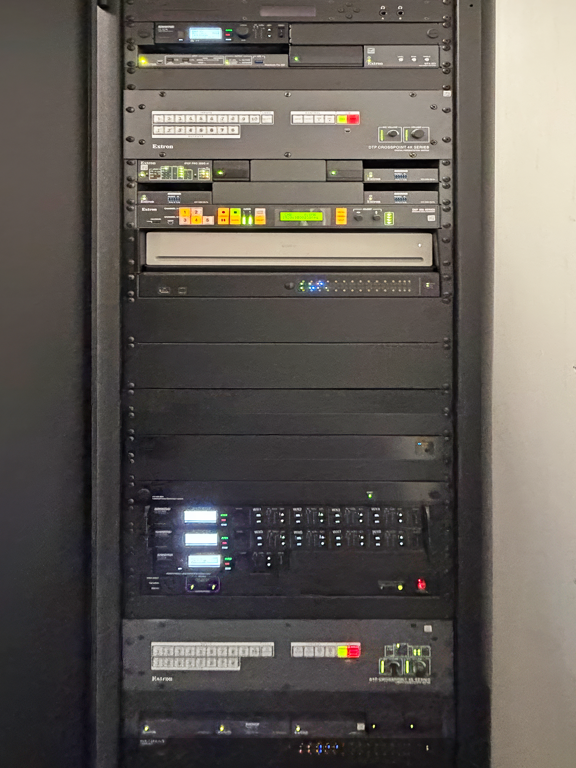 The equipment rack holds the two DTP CrossPoint switchers, the SMP 352 recorder, and other AV components. The layout keeps the system organized and easy to service.