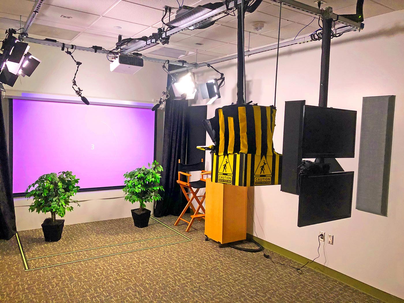 The Video Recording Room with curtains opened to reveal projection screen lowered and stage lights on, ready to record a presentation session. The configuration shown here is for a Green Screen Mode recording session. 