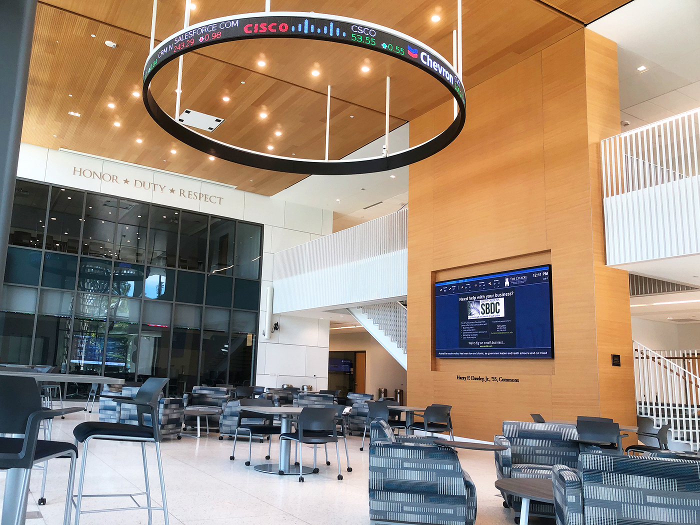 The public entrance to Bastin Hall is the Commons, a spacious venue where students gather to study, collaborate, meet, and attend group events. A circular stock ticker high above reflects the building's business focus. A videowall displays general interest messaging. The AV system includes a projector and screen that lower from the ceiling and a powerful sound system.