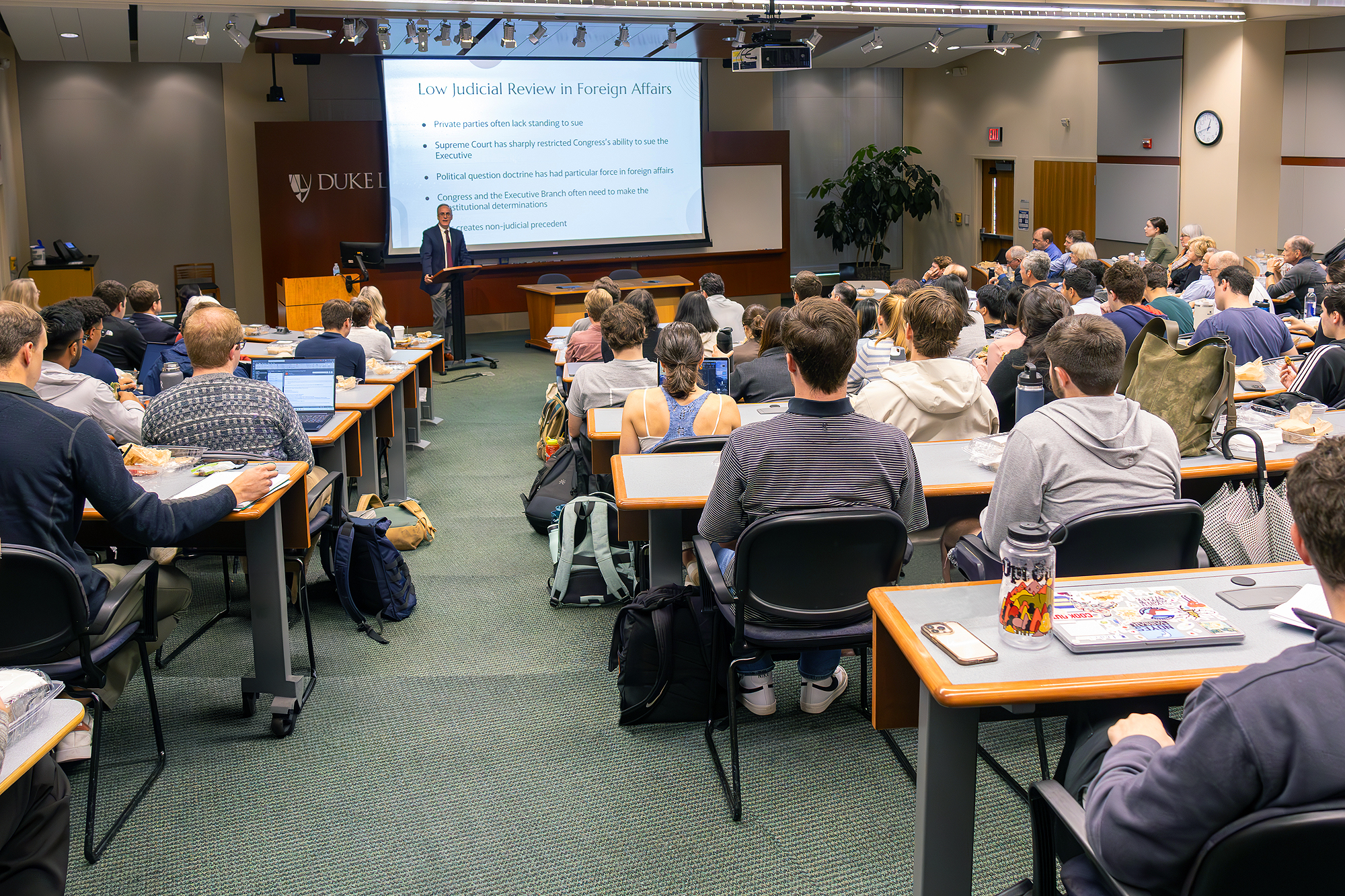 Room 3041 lecture hall with a projection screen,  plus side flat panel display. Accommodates 159 students and eight instructors.