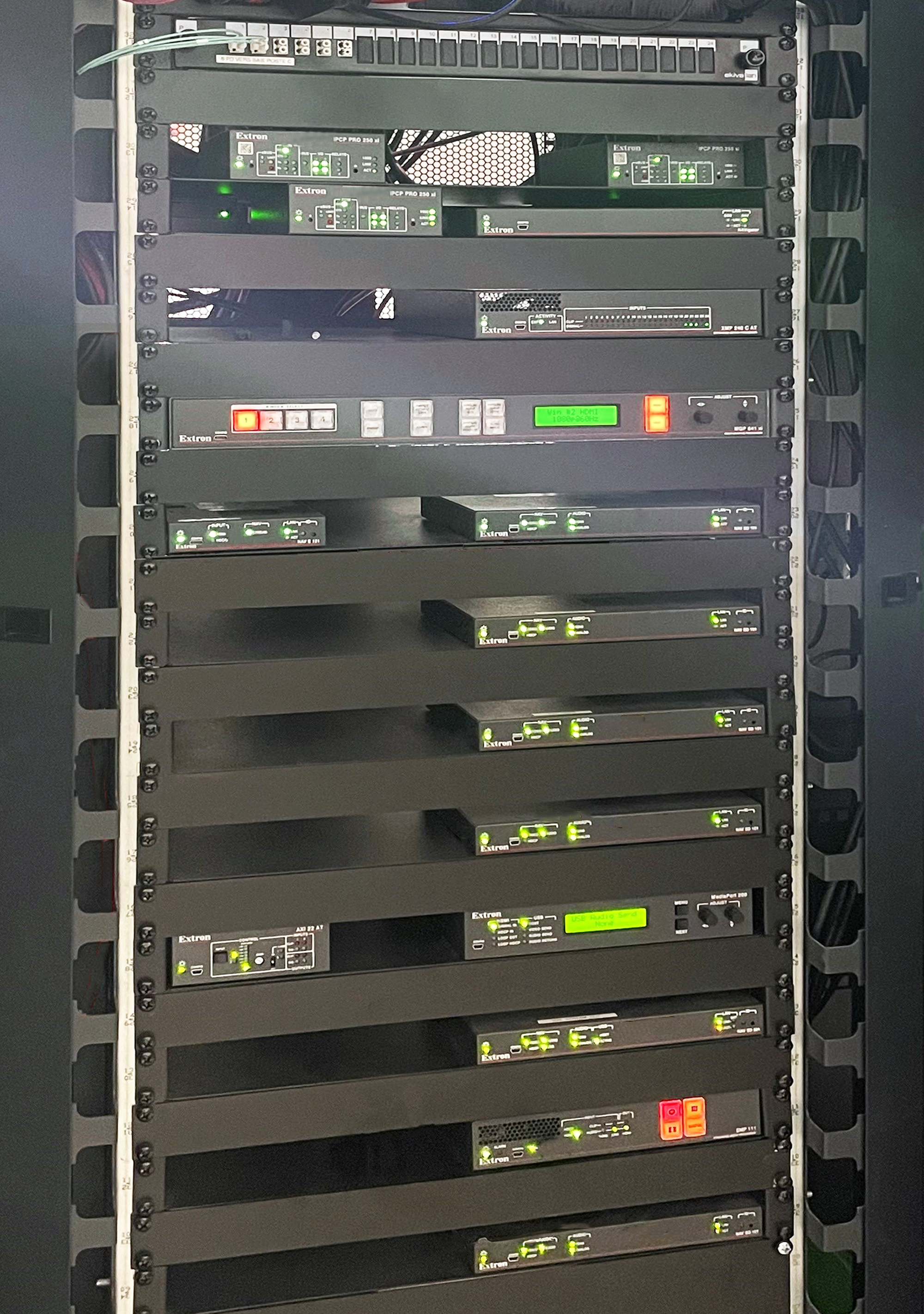 A centralized AV equipment rack houses Extron NAV endpoints and other AV system hardware. 