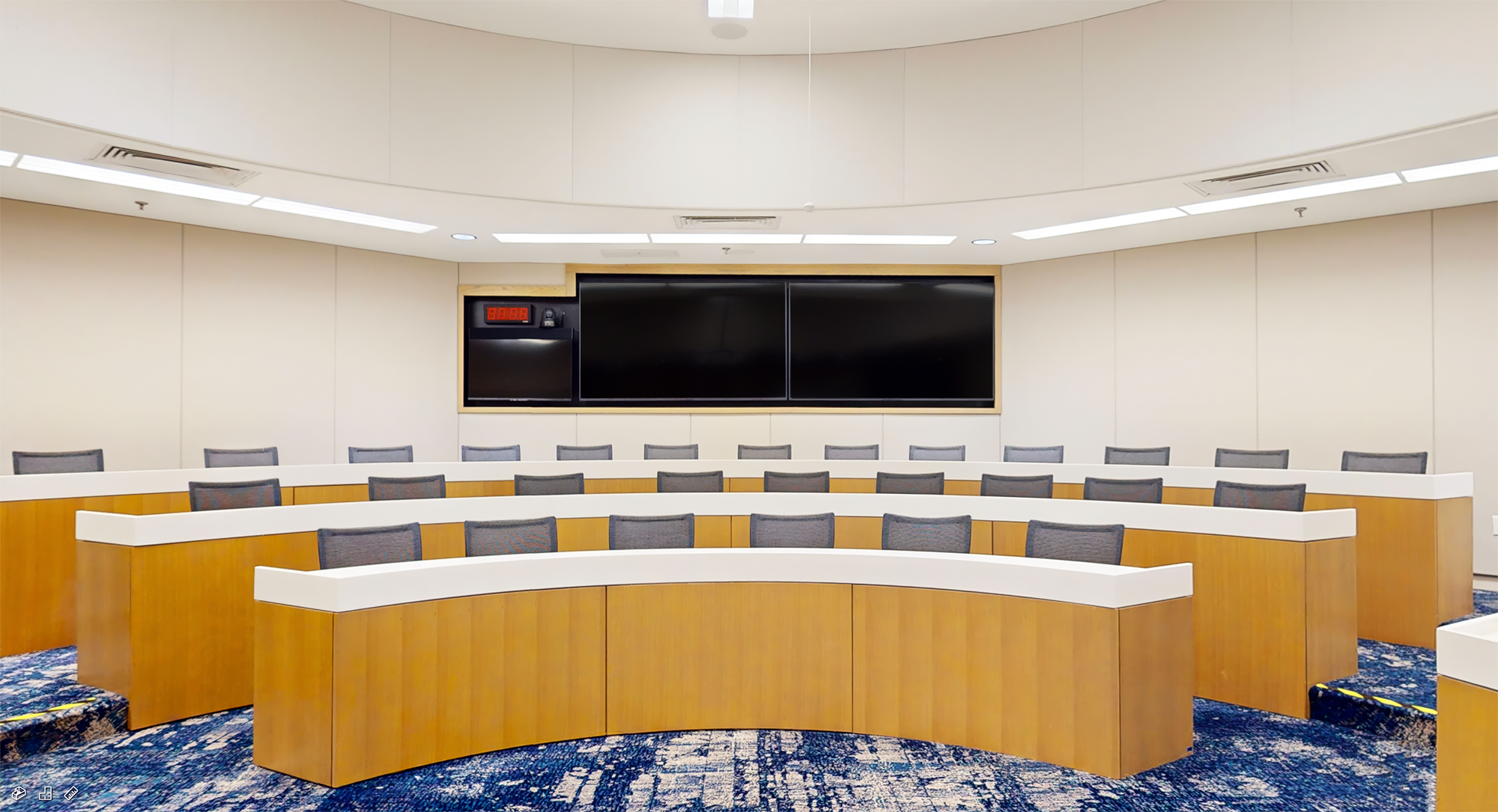 Vue du fond de la salle de classe Glaxo montrant les moniteurs de retour, l'horloge numérique, et la caméra PTZ avec suivi automatique. La salle de classe Executive est conçue à l'identique et est équipée de la même technologie audiovisuelle.