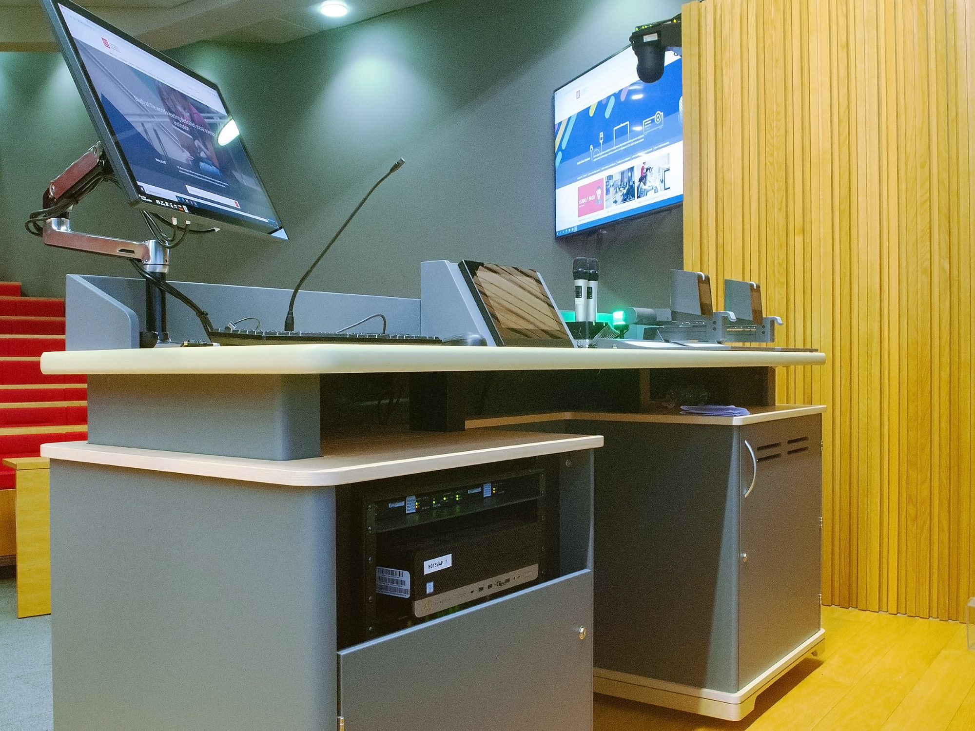 Le bureau du présentateur est équipé d'un moniteur sur bras articulé, d'un écran tactile TouchLink Pro, et de supports pour équipements audiovisuels intégrés pour un contrôle pratique et centralisé.