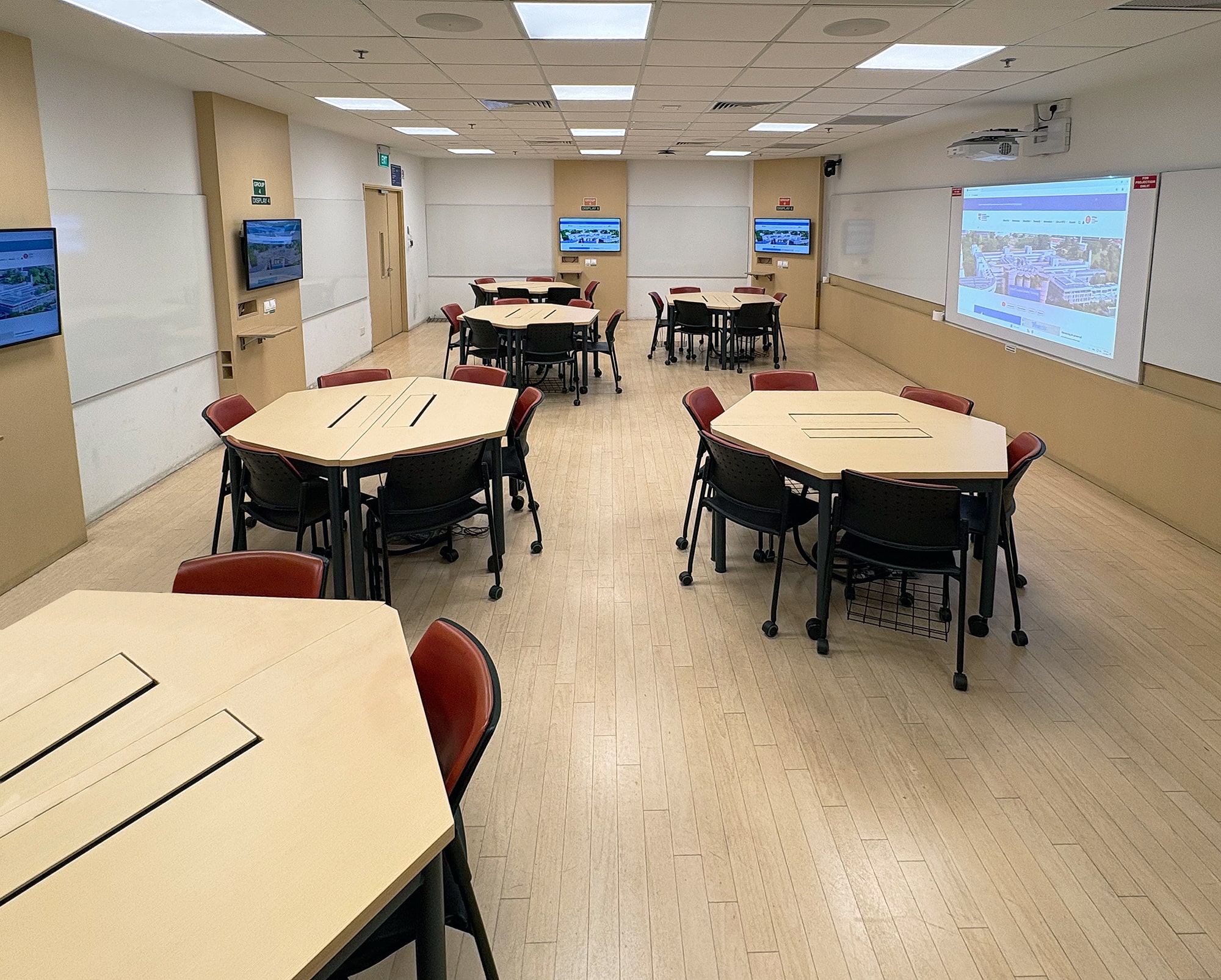 Vue d'une salle de tutorat standard, avec des tables hexagonales et des écrans sur tous les côtés pour répondre aux besoins de la classe inversée et de l'apprentissage collaboratif.