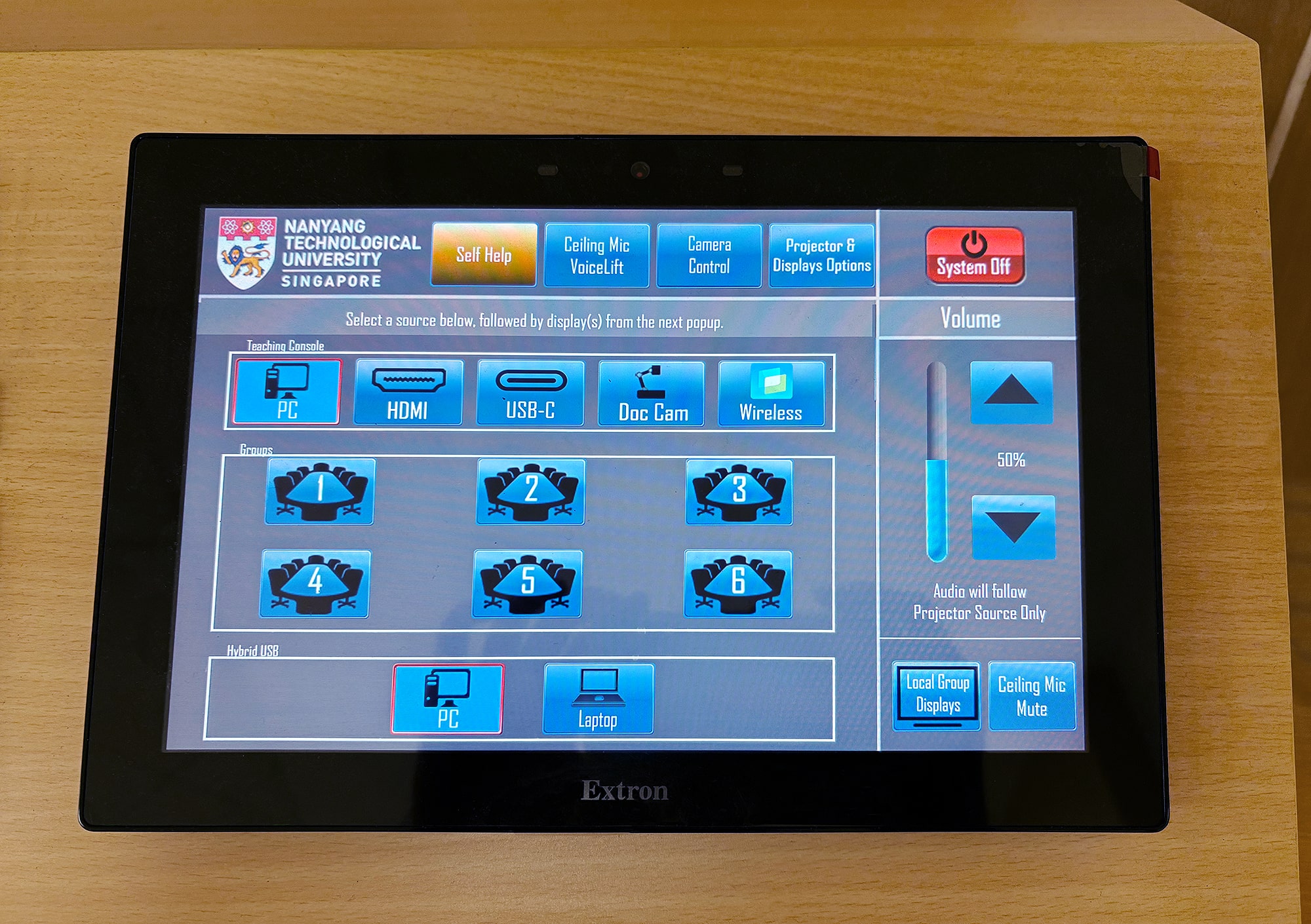 Vue rapprochée de l'écran tactile dans une salle de tutorat montrant l'interface graphique intuitive utilisée pour la sélection des sources, le contrôle du volume, et le dépannage.