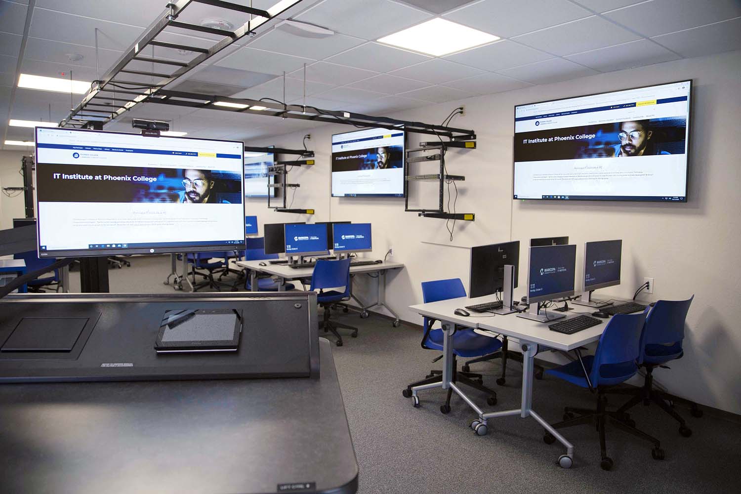 View of the networking lab, looking from the instructor station across the room at several of the student work pods and overhead network cable trays.