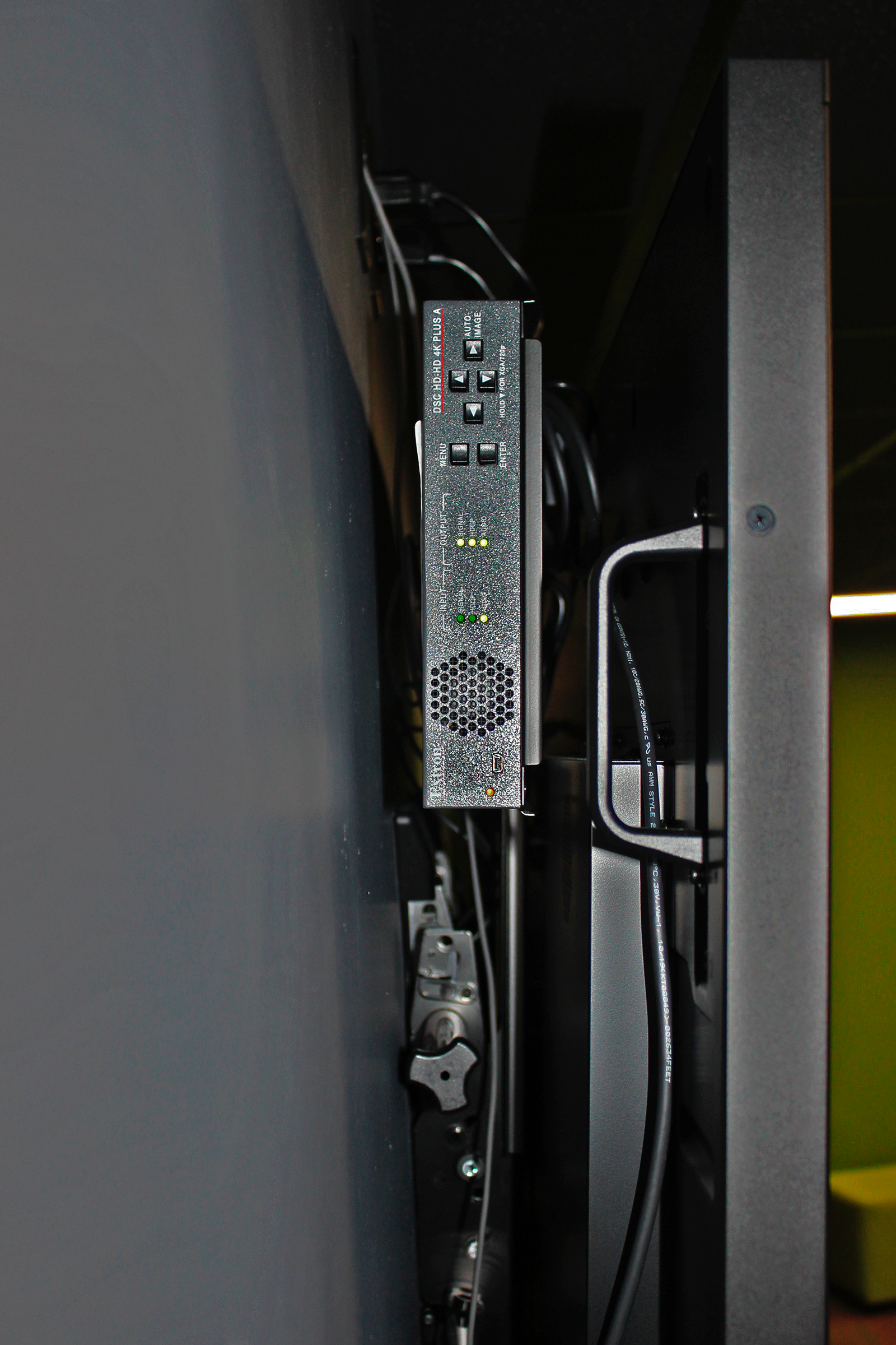 Le DSC HD‑HD 4K PLUS A installé derrière chaque écran mural redimensionne le signal 2560 x 1440 du PC vers la résolution native de l'écran. Le scaler associé à l'écran central désembedde également l'audio pour supporter le système sonore.