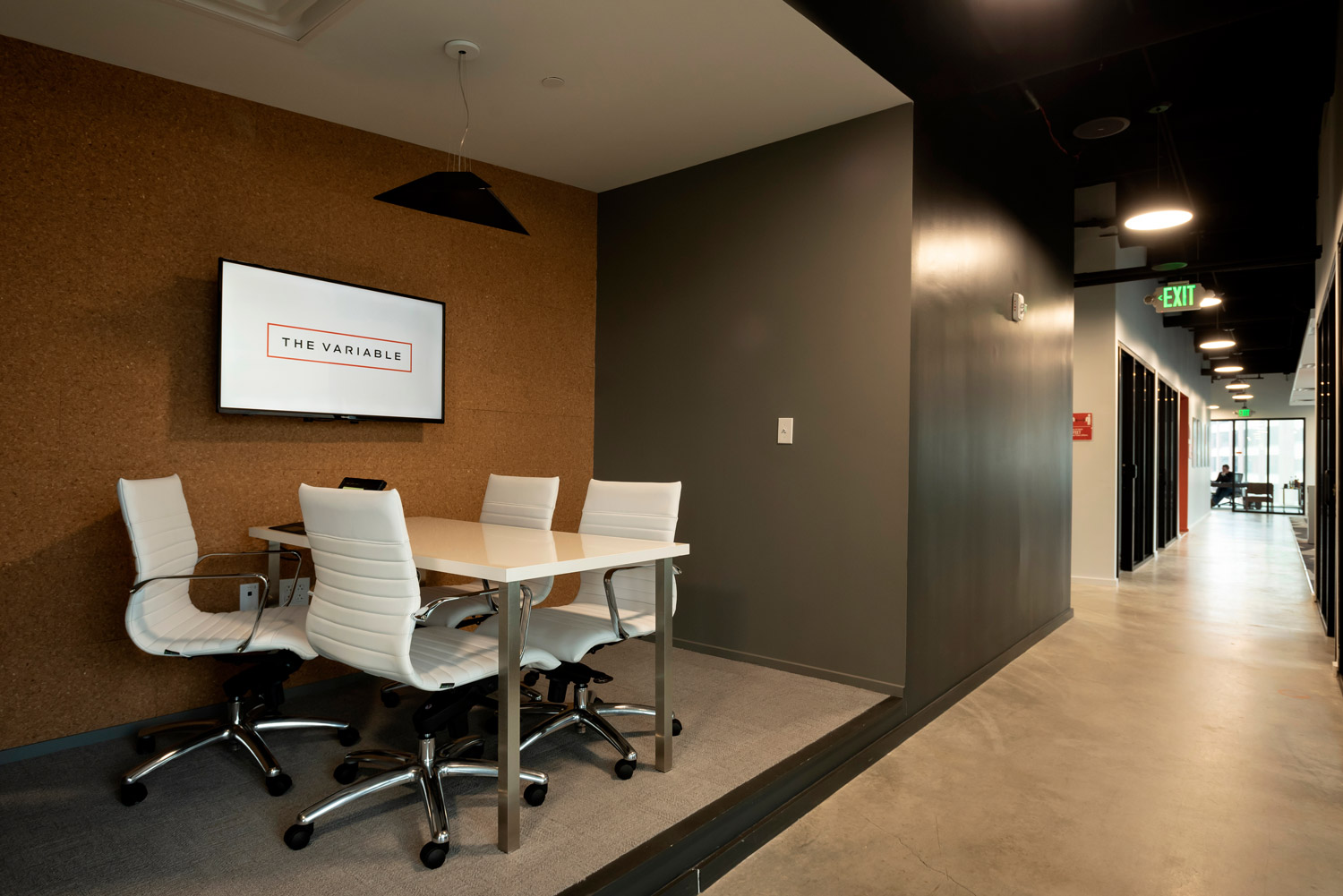 Vignette d'un couloir de bureau avec une table de conférence et un écran mural numérique.