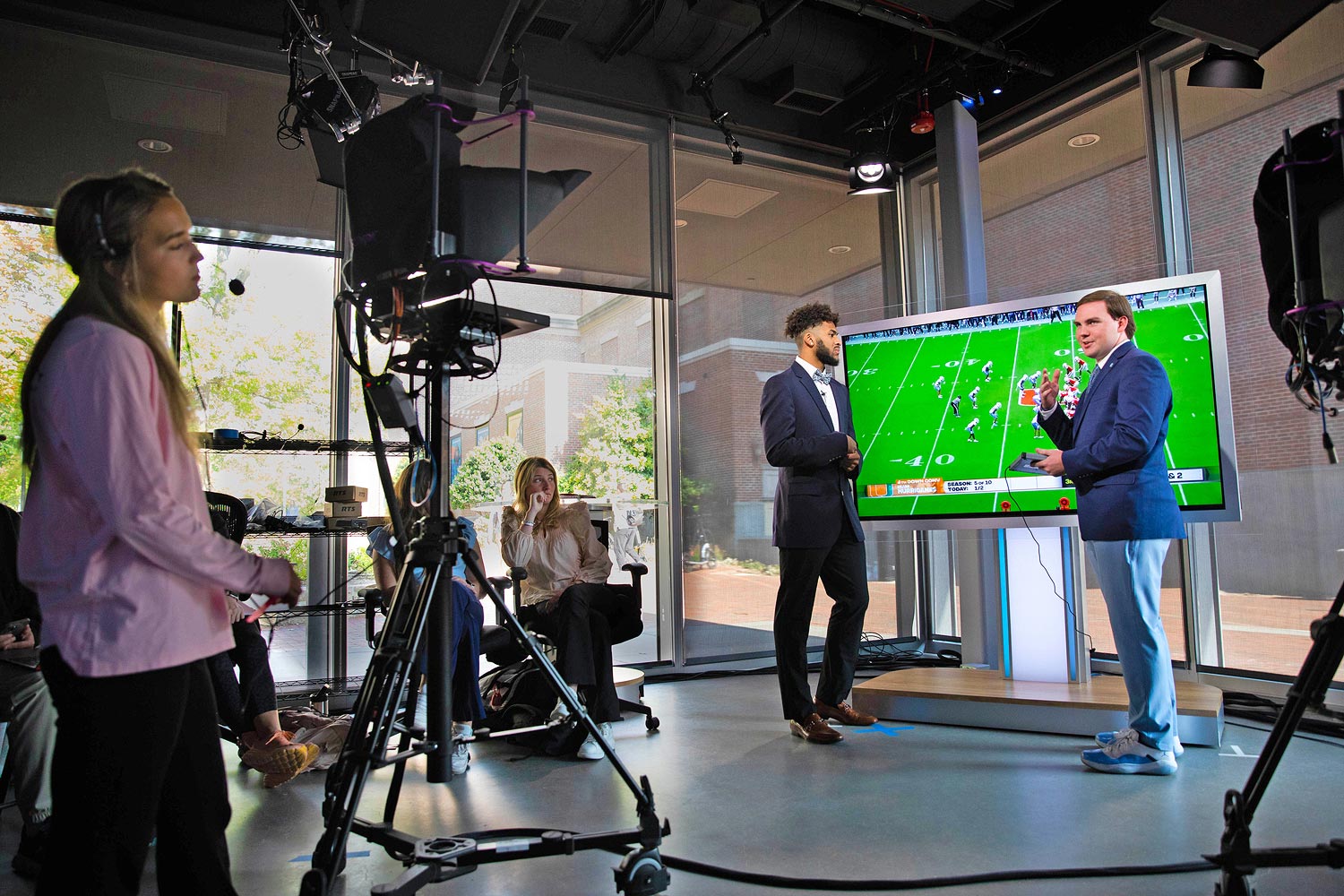 Miniaturanischt - Der Moderator des Sports Xtra-Programms kommentiert im James F. Goodman Broadcast-Studio ein American Football-Spiel mit einem der UNC-Spieler.