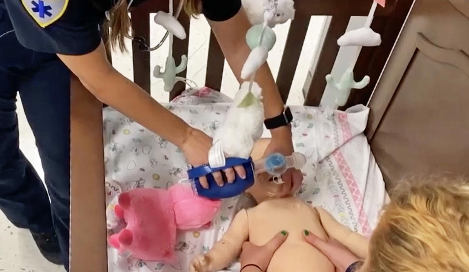 EMT students use a ventilator mask and chest compression to perform CPR on infant mannequin in crib at Wake Tech's EMS Simulation Suite.