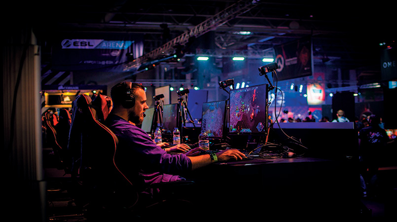 Участник киберспортивных игр за компьютером транслирует свой экран на установленные над ним мониторы.