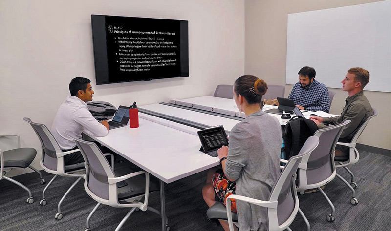 Una sala de colaboración con estudiantes de medicina reunidos alrededor de un dispositivo de visualización grande.