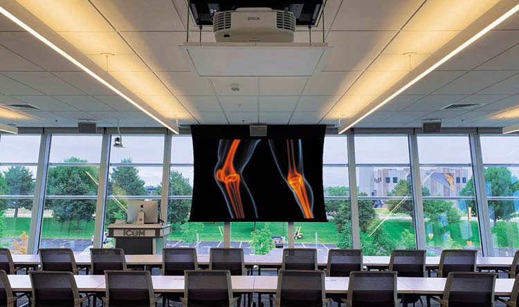 Ein Klassenraum mit einer Glaswand an einer chiropraktischen Schule, der mit einem Projektor und Bildschirm ausgestattet ist.